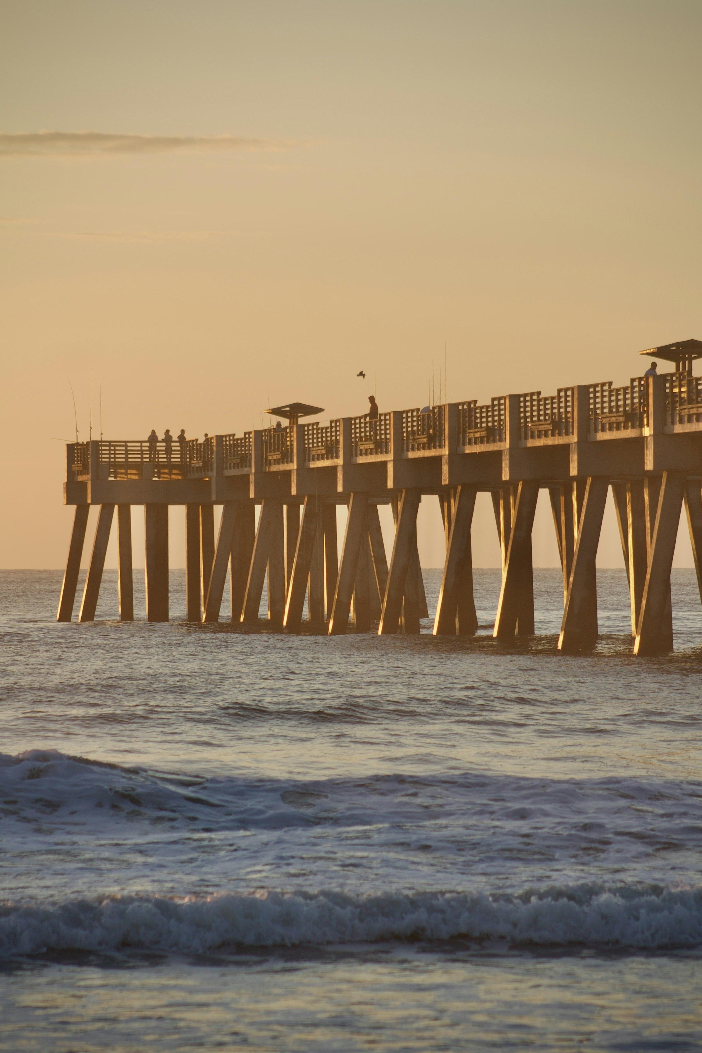 A fishing pier reaching into the ocean at golden hour